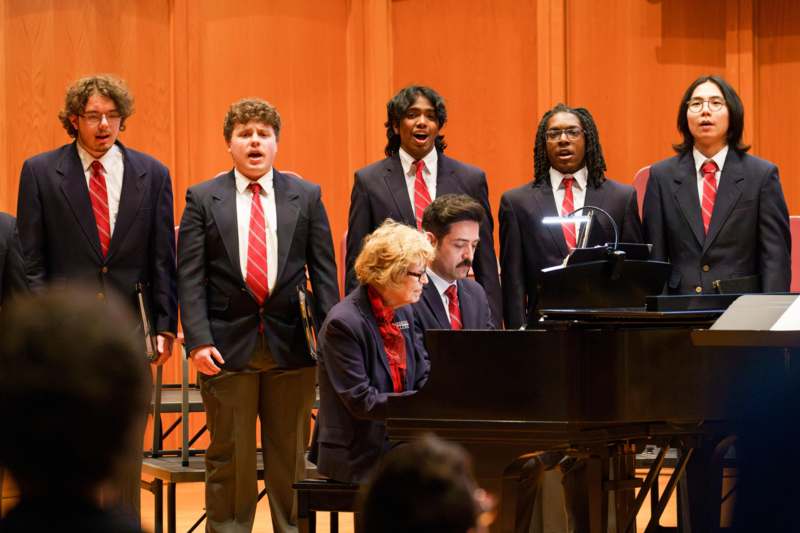 a group of people singing in front of a piano