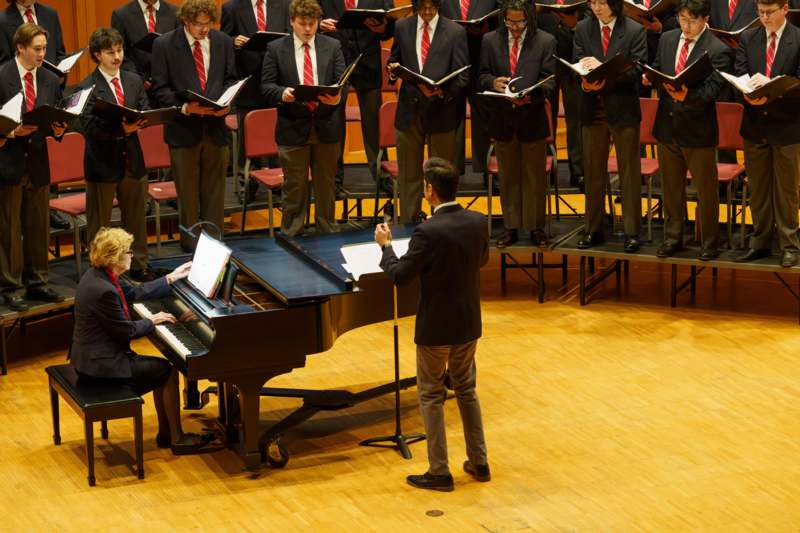 a group of people standing around a piano and a man holding a microphone