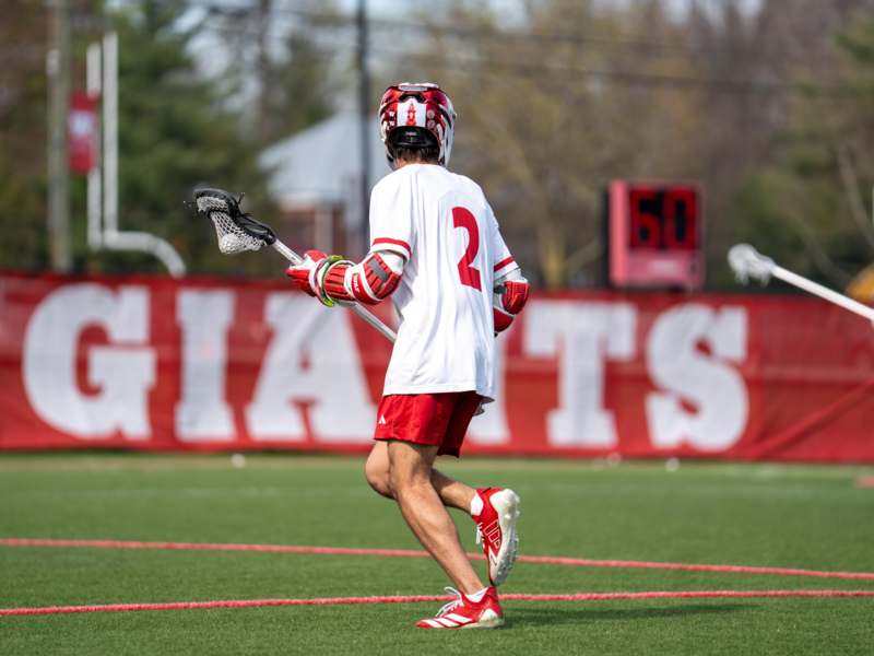 a man in a white shirt and red shorts holding a lacrosse stick