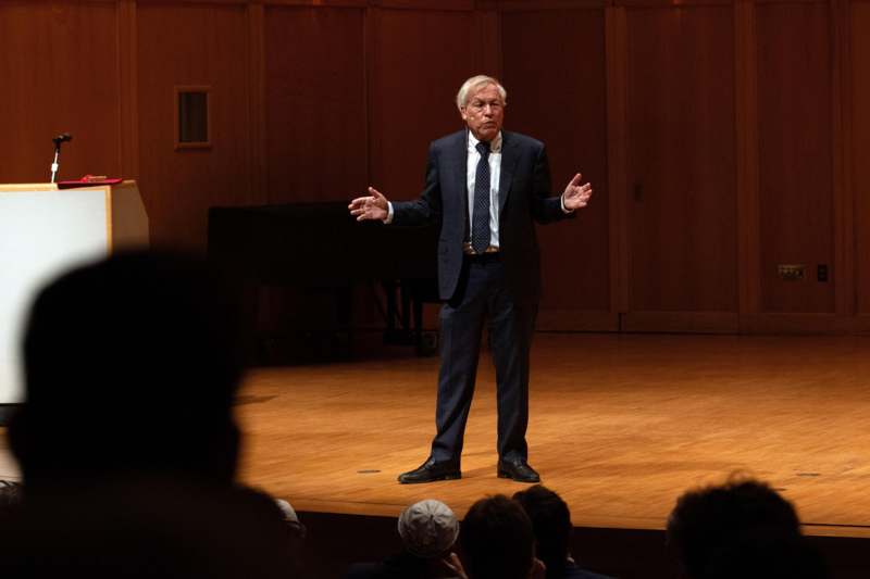 a man in a suit standing on a stage with his hands out