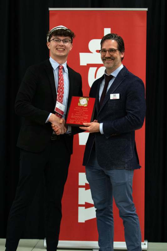 two men shaking hands with a red plaque