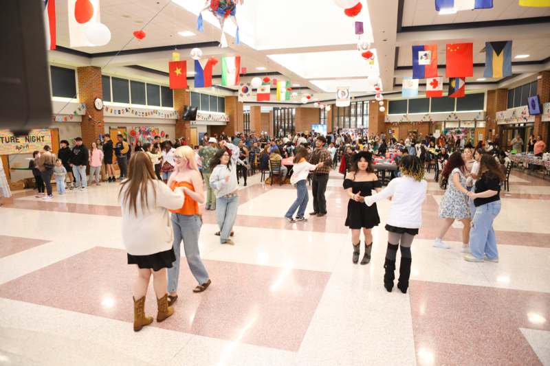 a group of people dancing in a room with flags and balloons