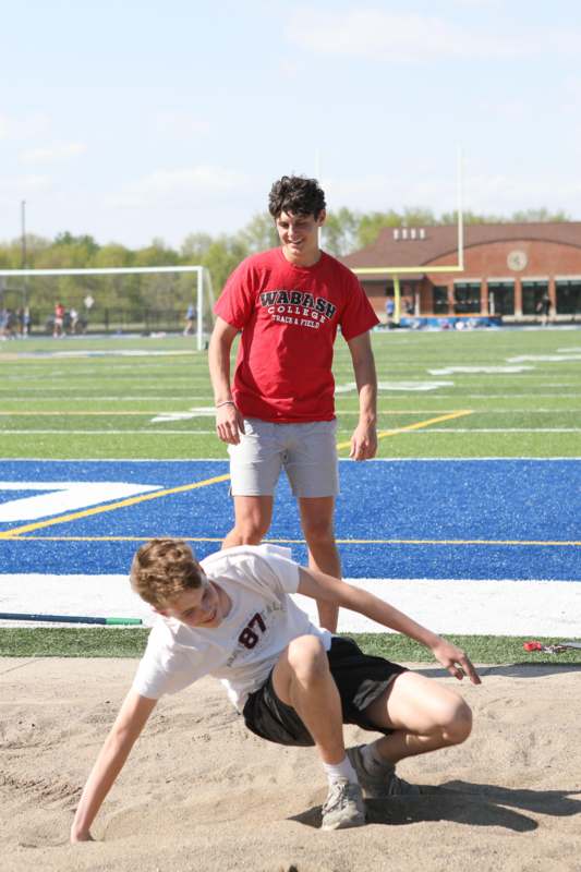 a man in a red shirt and white shirt playing long jump on a field