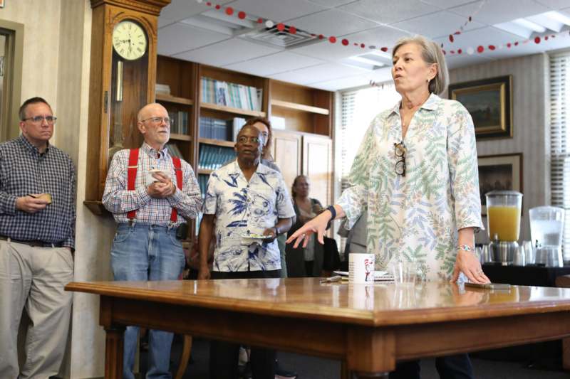 a woman standing in front of a table with people standing around