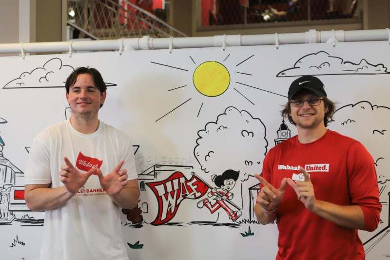 two men standing in front of a white sign