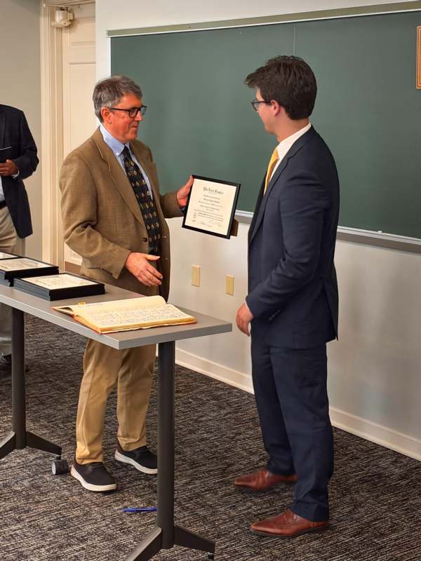 a man in suit holding a certificate to another man in a room