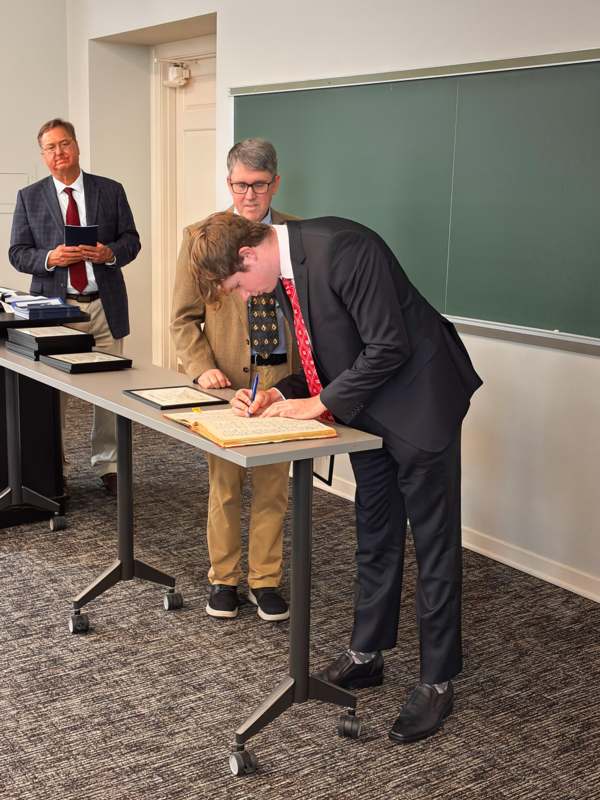 a group of men standing at a table signing papers