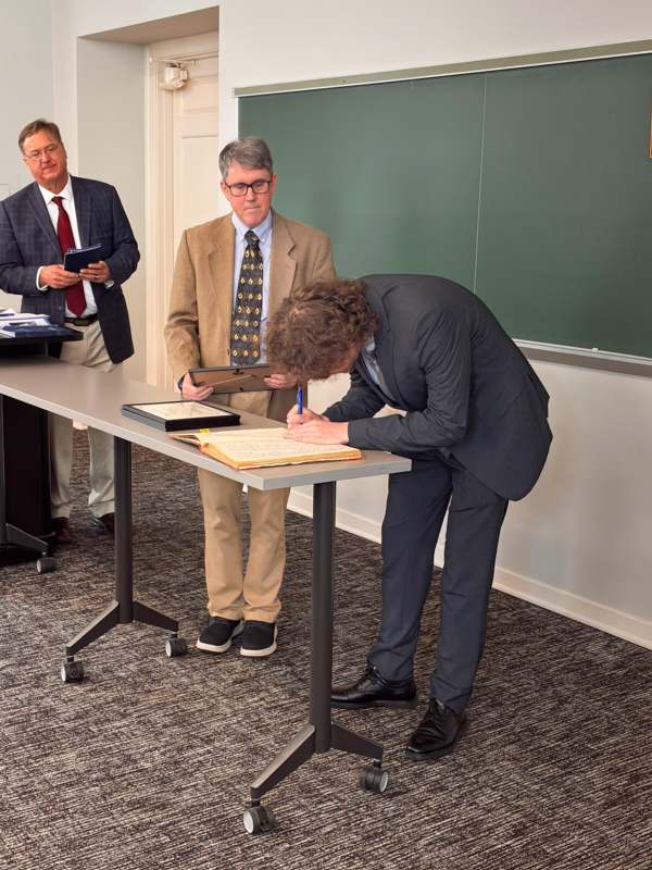 a group of men standing at a table writing on a book