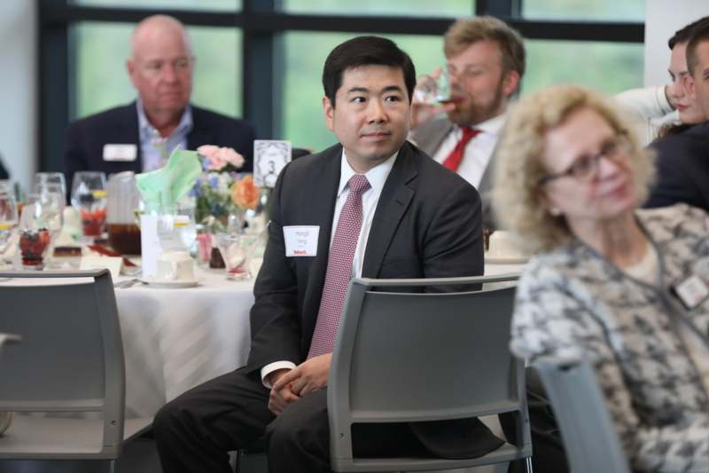 a man in suit sitting at a table with people in the background