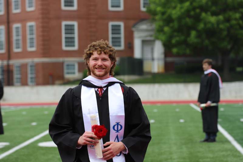a man in a graduation gown holding a rose and a diploma
