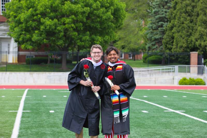 two men in graduation gowns on a football field