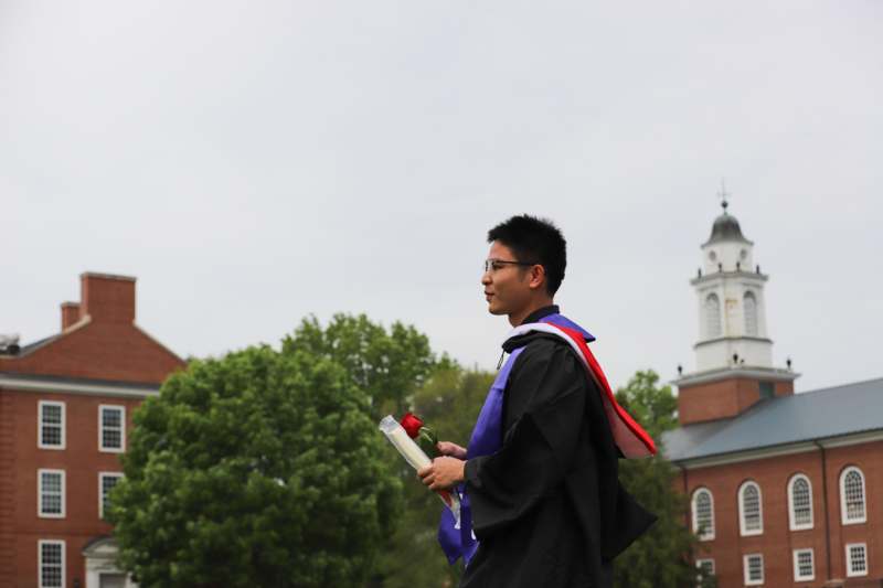 a man in a graduation gown holding a rose and a red rose