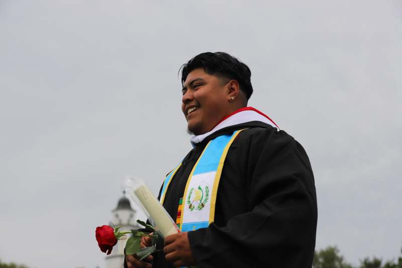 a man in a graduation gown holding a rose and a diploma