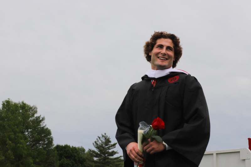 a man in a graduation gown holding a rose