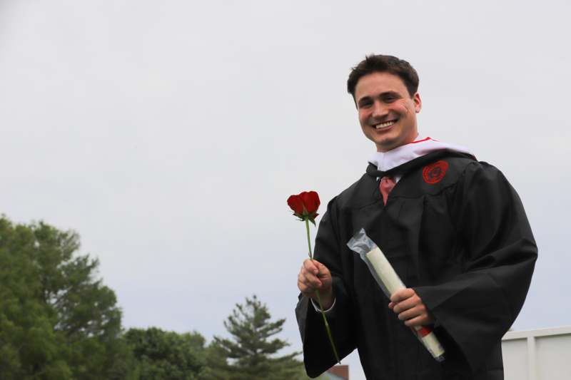 a man in a graduation gown holding a rose and diploma