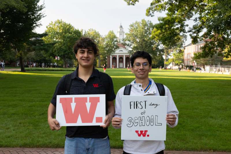 First Day of Classes-Fall 2026 - two men holding signs in front of a building