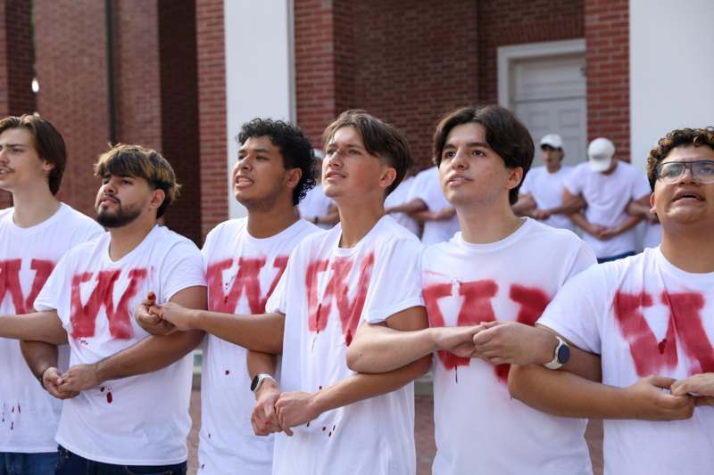 a group of men wearing white t-shirts with red letters on their shirts