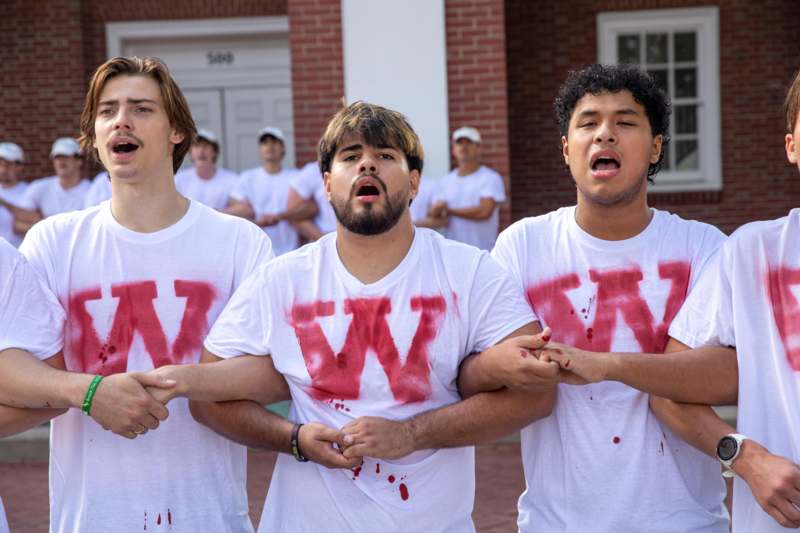 a group of men wearing white t-shirts with red letters