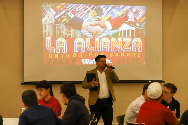 La Alianza Lunch and Tacos With Alumni - a man speaking into a microphone in front of a large projector screen